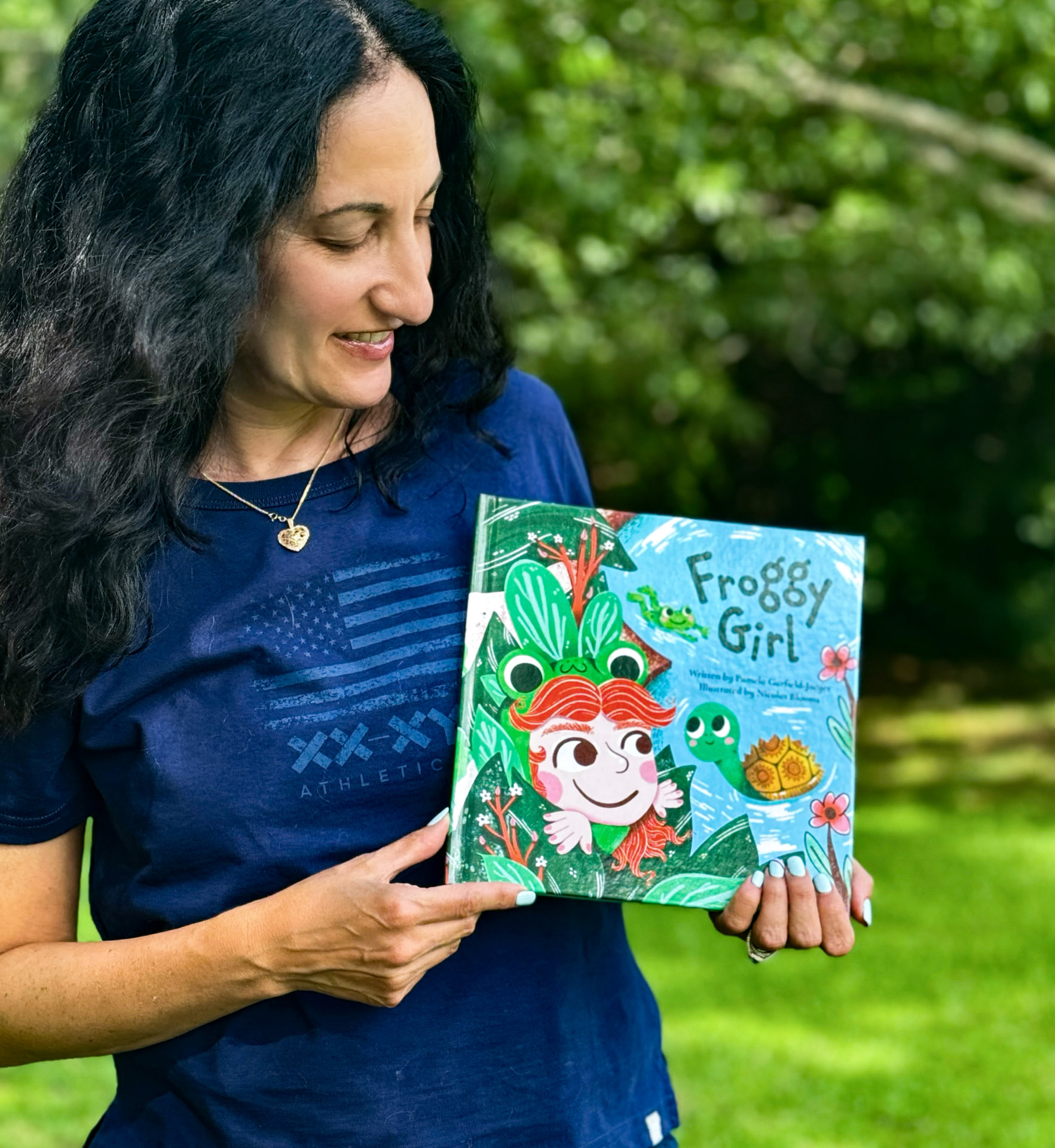 Pamela Garfield-Jaeger holding a hardback copy of her children's book Froggy Girl.